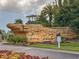 Community entrance with stone sign, vibrant flowers, and green landscaping under a cloudy sky at 4697 Golden Beach Ct, Kissimmee, FL 34746