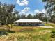 Exterior shot of home with white paint, metal roof, circular drive and mature trees at 11323 Kijik Trl, Groveland, FL 34736
