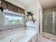 Soaking tub with decorative tile surround, a large window, and decorative shelves beside a glass-enclosed shower at 2939 Sera Bella Way, Kissimmee, FL 34744