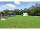 Expansive backyard featuring lush lawn, screened-in lanai, storage shed, and mature trees at 911 Mendoza Ln, Kissimmee, FL 34758
