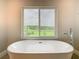 A soaking tub sits beneath a large window overlooking a lush, scenic outdoor landscape at 1870 Brentwood Ct, Davenport, FL 33837