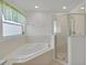 Bright bathroom features a bathtub, glass-door shower, and large window at 307 Balmoral Ct, Davenport, FL 33896