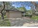 Paved driveway and a two-car garage with stone accents beneath mature trees at 9905 Nicoma Ln, Orlando, FL 32817