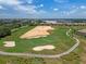Scenic aerial view of a golf course featuring sand traps, a putting green, and lush fairways surrounded by residential buildings at 1578 Slice Way, Davenport, FL 33896
