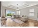Bright living room with hardwood floors, neutral decor, tray ceiling, modern light fixture, and sliding glass doors at 16049 Volterra Pt, Bella Collina, FL 34756