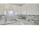 Well-lit kitchen features granite countertops, stainless sink, stylish backsplash, and white cabinetry at 505 Oak Dr, Tavares, FL 32778
