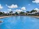 Community pool lined with lounging chairs and tropical landscaping under a blue sky at 12606 Old Plantation Ln, Orlando, FL 32824
