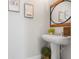 Powder room features a white pedestal sink, a round wood-framed mirror, and modern artwork on the walls at 15540 Blackbead St, Winter Garden, FL 34787