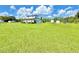Expansive green property featuring a modern white house with black trim and large field, set against a blue sky with scattered clouds at 4075 Packard Ave, St Cloud, FL 34772