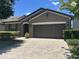 Single-story home showcases a brown exterior, a two-car garage, manicured landscaping, and a brick paver driveway at 2436 Gratia Pl, Casselberry, FL 32707