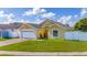 Charming yellow home with a two-car garage, green lawn, and a white fence at 5100 Violet Ln, Kissimmee, FL 34758