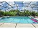 Screened-in pool with clear blue water, surrounded by lush greenery and blue sky with clouds at 344 Cherokee Ave, Haines City, FL 33844