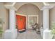 Welcoming front porch with tiled flooring, columns, and an bright orange entry door at 651 Regina Cir, Oakland, FL 34787