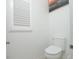 A simple powder room with toilet, white walls, trim and wainscoting, plus modern shuttered window and artwork at 1855 Treasure Cv, Kissimmee, FL 34747
