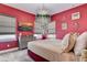 Bright bedroom with red walls, neutral carpet, decorative chandelier, and modern grey furniture at 7458 Gathering Dr, Kissimmee, FL 34747