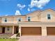 Charming two-story townhome featuring a two-car garage, tan siding, and a red tiled roof under a bright blue sky at 572 Bay Leaf Dr, Poinciana, FL 34759