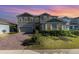 Charming two-story home with a manicured lawn, brick driveway, and beautiful sunset sky at 3200 Canna Lily Pl, Clermont, FL 34711