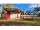 Red metal storage shed with a roll-up door and covered carport at 3720 Willis Rd, Mulberry, FL 33860