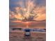 A serene beach scene with a chair facing the ocean and a vibrant sunset with sunrays through the clouds at 38 Seaside Dr, Ormond Beach, FL 32176