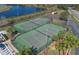 Aerial view of two tennis courts with lush landscaping, a lake view, and a parking lot in a well-maintained community at 3890 Wood Thrush Dr, Kissimmee, FL 34744