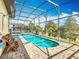 Clear, sunny view of a pool and spa inside of a screened-in enclosure with brick pavers and lush landscaping at 374 Villa Sorrento Cir, Haines City, FL 33844