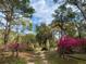 Serene view of the property entrance framed by lush trees, vibrant azaleas, and a rustic gate for privacy at 24605 Ne 177Th Ter, Fort Mc Coy, FL 32134