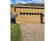 Tan two-car garage with brick paver driveway and green grass on the left at 15387 Avenue Of The Arbors, Winter Garden, FL 34787