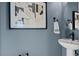 Chic powder room with blue walls, modern artwork, round mirror, and pedestal sink at 15113 Grove Lake Dr, Winter Garden, FL 34787