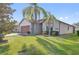 Inviting home exterior with lush green lawn, mature palm trees, and a brick-accented two-car garage at 474 Del Sol Ave, Davenport, FL 33837