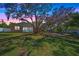 Large, grassy backyard with mature trees, a patio, and a fence under a colorful sky at dusk at 3688 Hurlbut Cir, Lake Wales, FL 33898