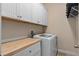 Well-organized laundry area with white cabinets, butcher block counter, and modern washing machine at 9170 Tavistock Lakes Blvd, Orlando, FL 32827