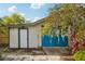 A detached garage with a white door, blue garage doors, and a flowering tree sits in the back yard at 515 Frank Lloyd Wright Way, Lakeland, FL 33803