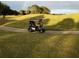A black golf cart parked on a paved cart path with a grassy golf course and rainbow in the background at 3533 Roanoke St, The Villages, FL 32162