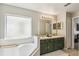 Bright bathroom showcasing a garden tub and double vanity with dark green cabinetry and gold hardware at 440 Langham Dr, Davenport, FL 33897