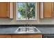 Close-up of kitchen sink under a window with wooden cabinets and dark countertops at 2415 Brownwood Dr, Mulberry, FL 33860