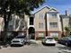 View of a tan and white two-story condo with red brick foundation and parked cars at 13103 Mulberry Park Dr # 833, Orlando, FL 32821