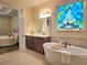 Elegant bathroom with soaking tub, dual sink vanity, and charming stained-glass window at 13525 Gorgona Isle Dr, Windermere, FL 34786