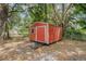 Exterior view of a red storage shed in a backyard setting surrounded by mature trees and fencing at 1313 Periwinkle Ct, Lakeland, FL 33811