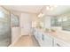 Bright bathroom with double vanity, large mirror, shower with glass door, and natural wood-look floors at 7682 Fairfax Dr, Kissimmee, FL 34747