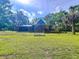 Expansive backyard with a dark blue house featuring a covered patio, surrounded by mature trees and greenery at 2900 Cr 415, Lake Panasoffkee, FL 33538