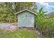 A small outbuilding with a wooden door sits amongst the trees and lush plants, and a partly cloudy sky at 728 Trenton Rd, Lakeland, FL 33815