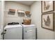 Bright laundry room features a washer, dryer, wire shelving with decorative baskets, and botanical art prints at 774 Ambleside Ave, Haines City, FL 33844