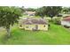 Aerial view of a yellow single-Gathering home with a well-kept lawn, sliding glass doors, and a tile roof at 413 Bay Leaf Dr, Poinciana, FL 34759