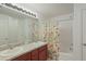 Bright bathroom with double sinks, wood cabinets, large mirror, and shower with floral curtain at 109 James Cir, Lake Alfred, FL 33850