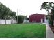 Wide backyard with red metal building, well-maintained lawn, mature trees and a white fence at 1423 Spruce N Rd, Lakeland, FL 33809