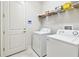 Clean laundry room featuring white washer and dryer with storage shelf and a white door at 7991 Lake James Blvd, Lakeland, FL 33810