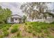 Home's backyard with an aging home, overgrown lawn, and mature tree at 303 Clayton Rd, Auburndale, FL 33823