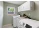 Bright laundry room with white cabinetry, tile floors, a window, and modern washer and dryer appliances at 722 Swaying Palm Dr, Apopka, FL 32712