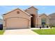 Beige single-story home featuring an attached two-car garage and manicured landscaping at 547 Sardinia Cir, Davenport, FL 33837
