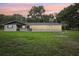 Rear exterior view of a home with a screened porch and lush green yard at sunset at 5525 Tillman Rd, Lakeland, FL 33810